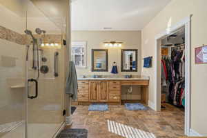Bathroom with double vanity, stone finish flooring, a stall shower, and a walk in closet