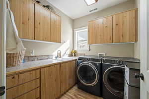Laundry room with cabinet space, separate washer and dryer, and light wood-style floors
