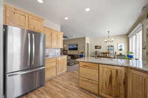 Kitchen with light wood finish cabinets, freestanding refrigerator, light stone countertops, light wood-style flooring, and suspended lighting