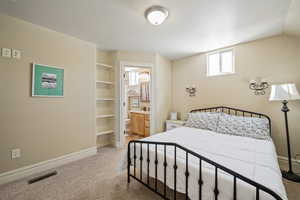 Bedroom featuring ensuite bathroom, light carpet, and vaulted ceiling