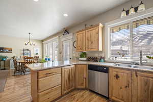 Kitchen with stainless steel dishwasher, suspended lighting, light wood-style floors, a peninsula, and light wood finish cabinetry