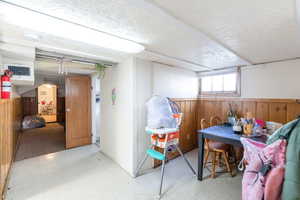 Basement featuring wood walls, tile patterned floors, a wainscoted wall, and a textured ceiling