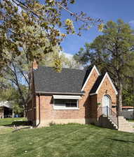 View of front of house featuring a front lawn, roof with shingles, brick siding, and a chimney