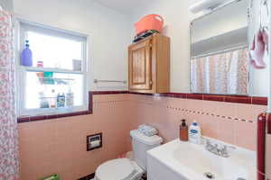 Bathroom with a shower with shower curtain, vanity, wainscoting, and tile walls