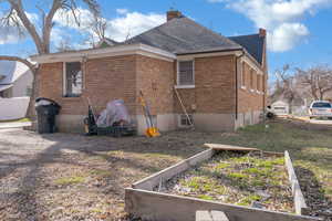 View of main home's exterior featuring a chimney, brick siding, roof with shingles, and a garden