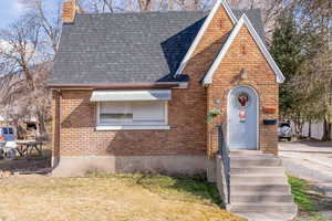 English style home with brick siding, a shingled roof, a chimney, and a front lawn