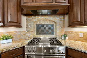 Kitchen featuring high end stove, light stone counters, and tasteful backsplash