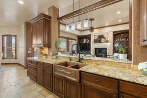Kitchen with decorative light fixtures, light stone counters, stone tile floors, a glass covered fireplace, and open floor plan