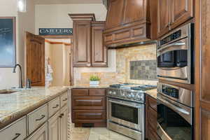 Two tone kitchen with light stone counters, stainless steel appliances, tasteful backsplash, stone tile flooring, and two tone cabinets
