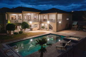 Rear view of house with a patio, a balcony, stucco siding, an outdoor pool, and an in-ground hot tub