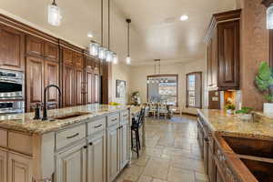 Kitchen with decorative light fixtures, stone tile floors, light stone counters, a kitchen island with sink, and a kitchen breakfast bar