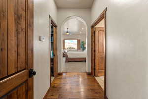 Corridor featuring wood-type flooring, arched walkways, a textured wall, and recessed lighting