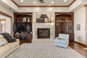 Living area featuring a premium fireplace, hardwood / wood-style floors, recessed lighting, a tray ceiling, and crown molding