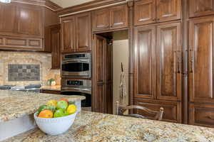 Kitchen featuring light stone counters, decorative backsplash, double oven and HIDDEN PANTRY