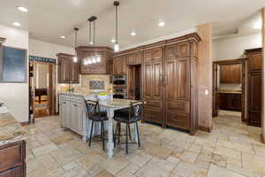 Kitchen featuring a breakfast bar, hanging light fixtures, a kitchen island, light stone countertops, and stone tile flooring