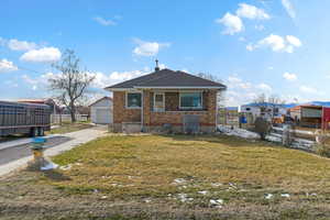 View of front facade featuring brick siding, a detached garage, an outbuilding, and a shingled roof