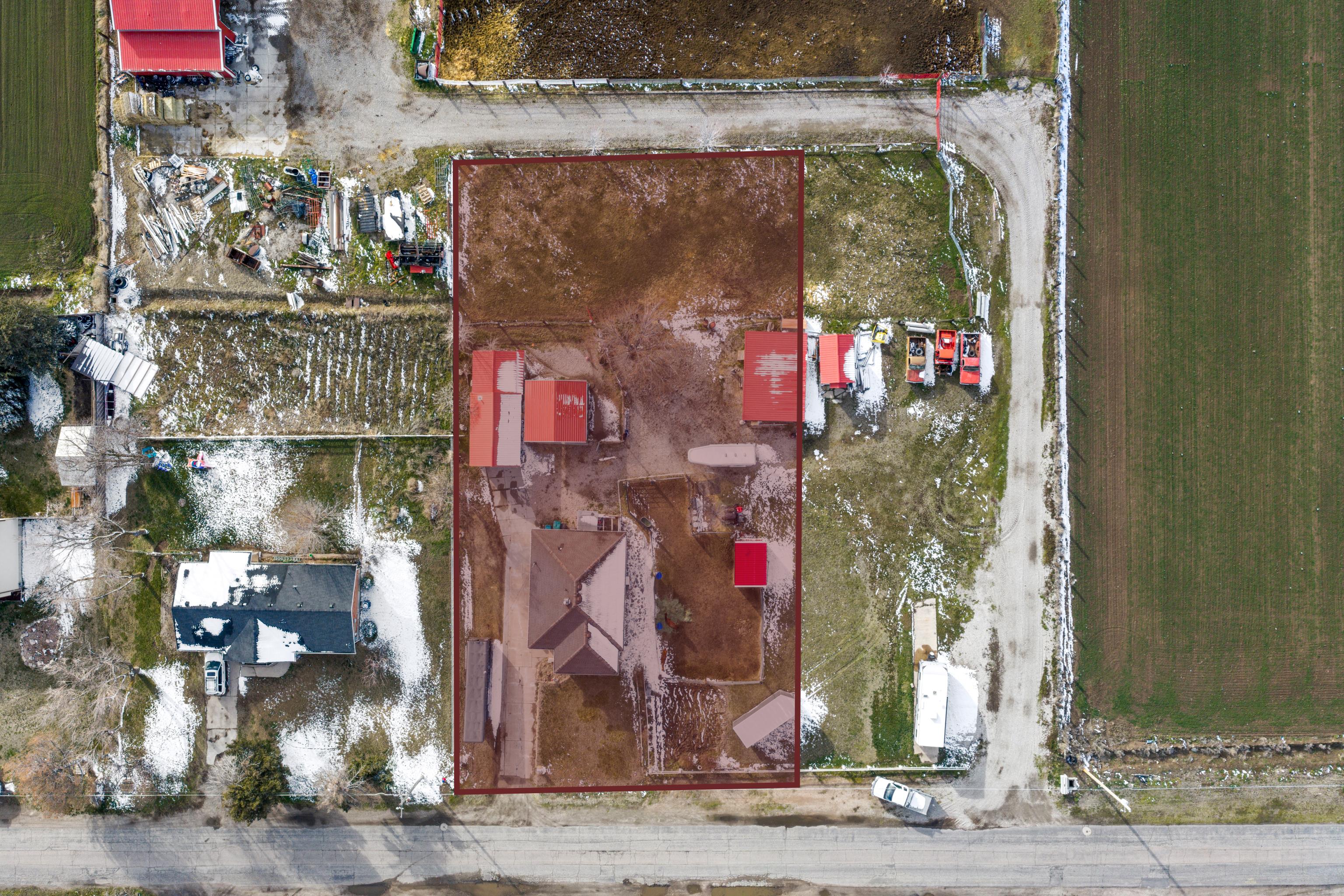 Expansive property featuring a main residence with a brown shingle roof, multiple outbuildings with red metal roofs, and direct road frontage
