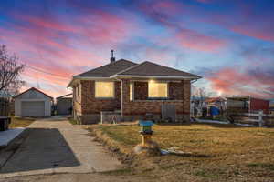 Bungalow-style home with brick siding, an outbuilding, a detached garage, a shingled roof, and concrete driveway
