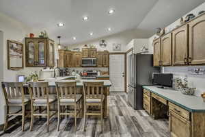 Kitchen with lofted ceiling, wood finish cabinets, light countertops, a kitchen breakfast bar, and stainless steel appliances