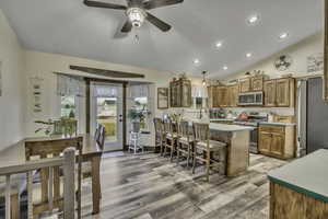 Kitchen featuring glass insert cabinets, a ceiling fan, light countertops, stainless steel appliances, and a kitchen breakfast bar