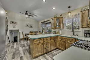 Kitchen with wood finish cabinetry, freestanding refrigerator, light countertops, and lofted ceiling