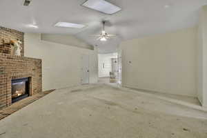 Unfurnished living room with carpet floors, ceiling fan, and a brick fireplace