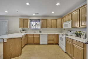 Kitchen with a peninsula, white appliances, light countertops, recessed lighting, and light wood finish cabinetry
