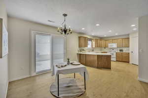 Kitchen with light countertops, white appliances, a peninsula, light wood-type flooring, and hanging lights