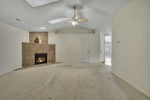 Unfurnished living room with carpet floors, a ceiling fan, lofted ceiling, a brick fireplace, and a skylight