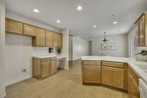 Kitchen with a peninsula, light countertops, suspended lighting, light wood finished floors, and white dishwasher
