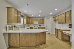 Kitchen featuring light countertops, white appliances, a peninsula, light wood finished floors, and recessed lighting