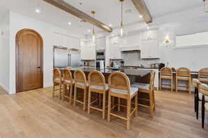 Kitchen with dual tone cabinets, arched walkways, a large island with sink, a kitchen bar, and light wood-style flooring