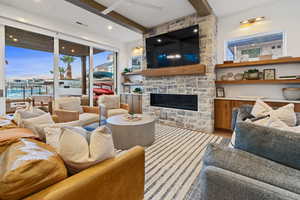 Living area featuring beam ceiling, a fireplace, wood finished floors, a ceiling fan, and plenty of natural light