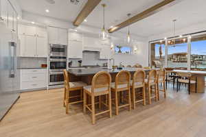 Kitchen with dual tone cabinetry, a large island with sink, light wood finished floors, stainless steel appliances, and backsplash