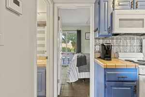 Kitchen featuring blue cabinets, tile countertops, white appliances, ornamental molding, and dark tile patterned floors