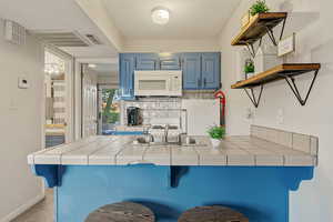 Kitchen with blue cabinetry, a kitchen bar, open shelves, and tile counters