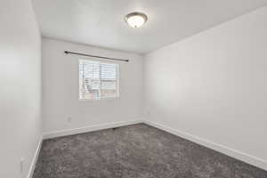 Empty room featuring dark colored carpet and a textured ceiling