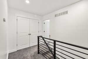 Hallway with dark carpet and an upstairs landing