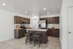 Kitchen featuring stainless steel appliances, a breakfast bar, an island with sink, dark wood finish cabinets, and a textured ceiling
