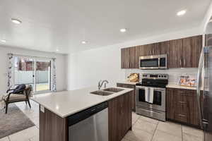 Kitchen with stainless steel appliances, modern cabinets, dark wood finish cabinetry, light tile patterned floors, and light stone counters