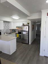 Kitchen with a textured ceiling, stainless steel appliances, white cabinets, light countertops, and ornamental molding
