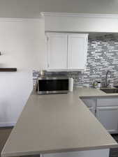Kitchen featuring ornamental molding, stainless steel microwave, white cabinets, backsplash, and a textured ceiling