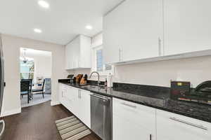 Kitchen featuring dark stone countertops, stainless steel dishwasher, white cabinets, and plenty of natural light