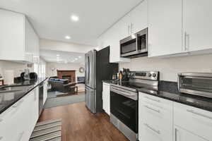 Kitchen with stainless steel appliances, white cabinets, dark stone countertops, a fireplace, and dark wood-style flooring