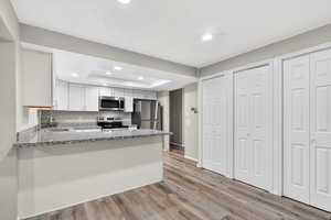 Kitchen with white cabinetry, recessed lighting, light wood-type flooring, stainless steel appliances, and a tray ceiling