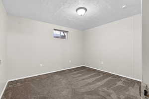 Empty room featuring a textured ceiling and dark carpet