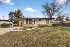 View of front facade with brick siding, driveway, a chimney, and a carport