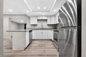 Kitchen with stainless steel appliances, recessed lighting, light stone countertops, a peninsula, and light wood-style flooring