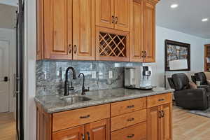 Kitchen featuring light wood-style floors, dark stone counters, wood finish cabinetry, tasteful backsplash, and open floor plan