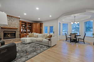 Living area featuring light wood-type flooring, a brick fireplace, a tray ceiling, and hanging lights